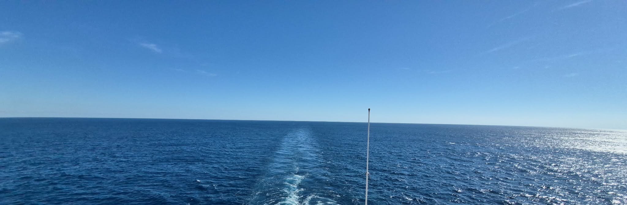 Ship's wake trailing across open ocean at sunset